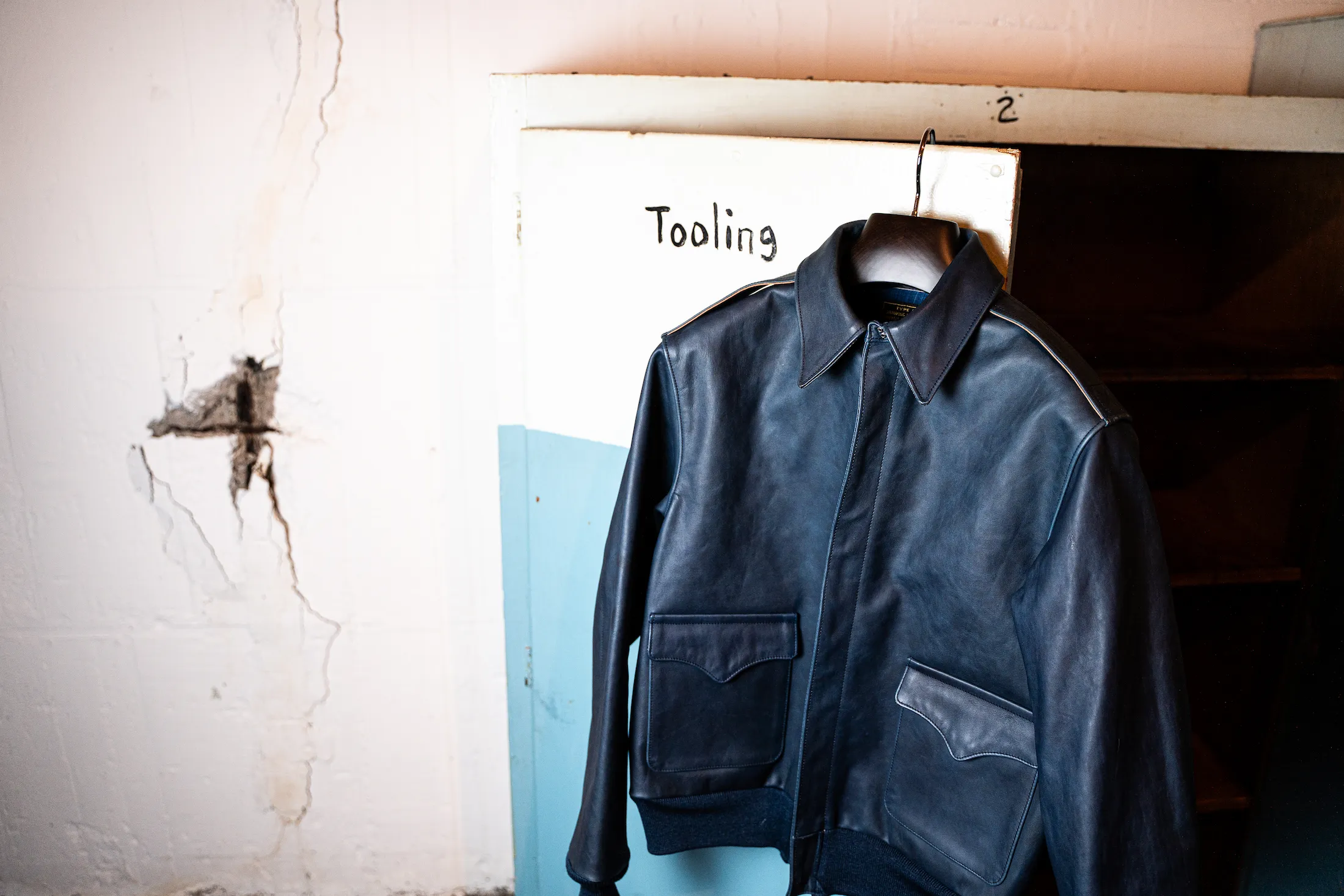 白い背景に映える、ハンガーにかけられたブルーのレザージャケット